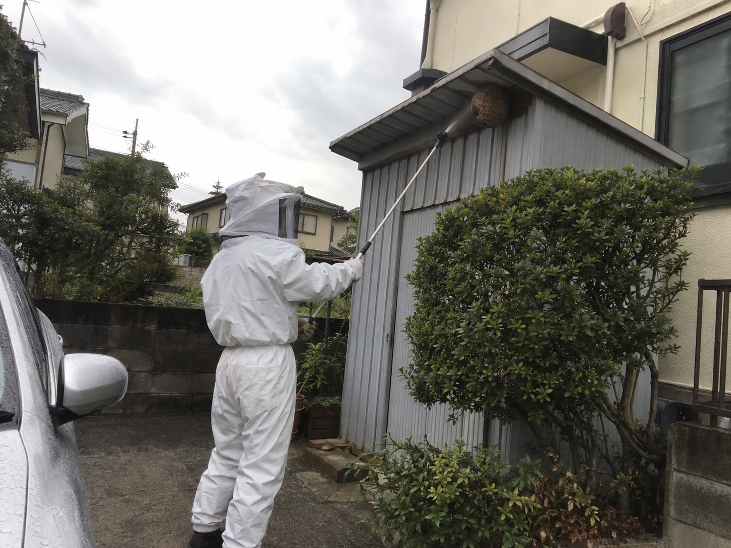 防護服を着た作業者が収納庫の軒下を確認する様子
