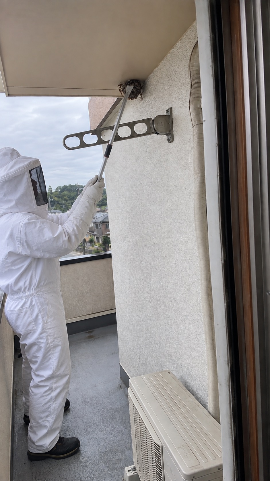 防護服でベランダ軒下の蜂の巣を処理している作業中の様子