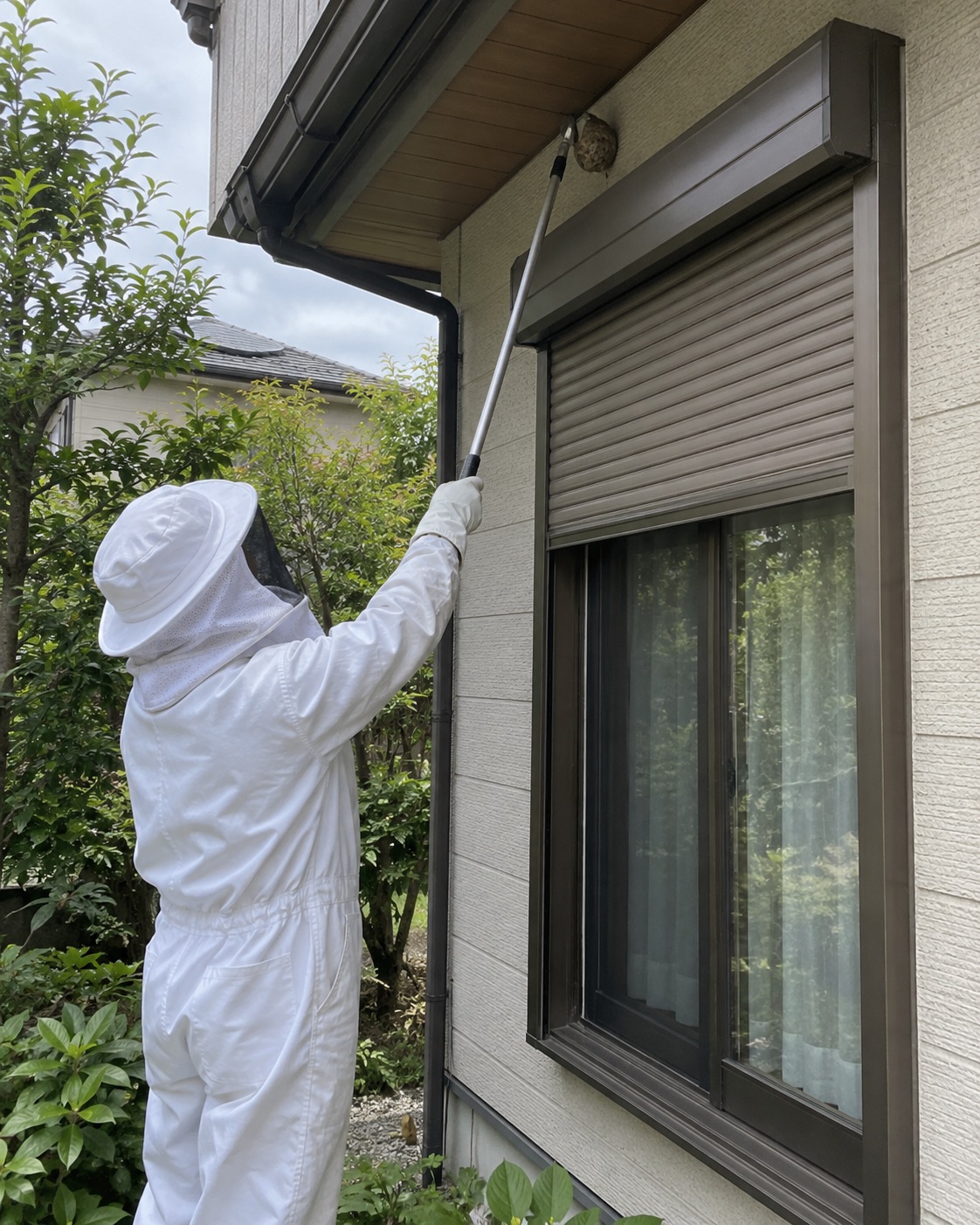 防護服の作業員が窓から距離を取り長い道具で巣を処理する様子