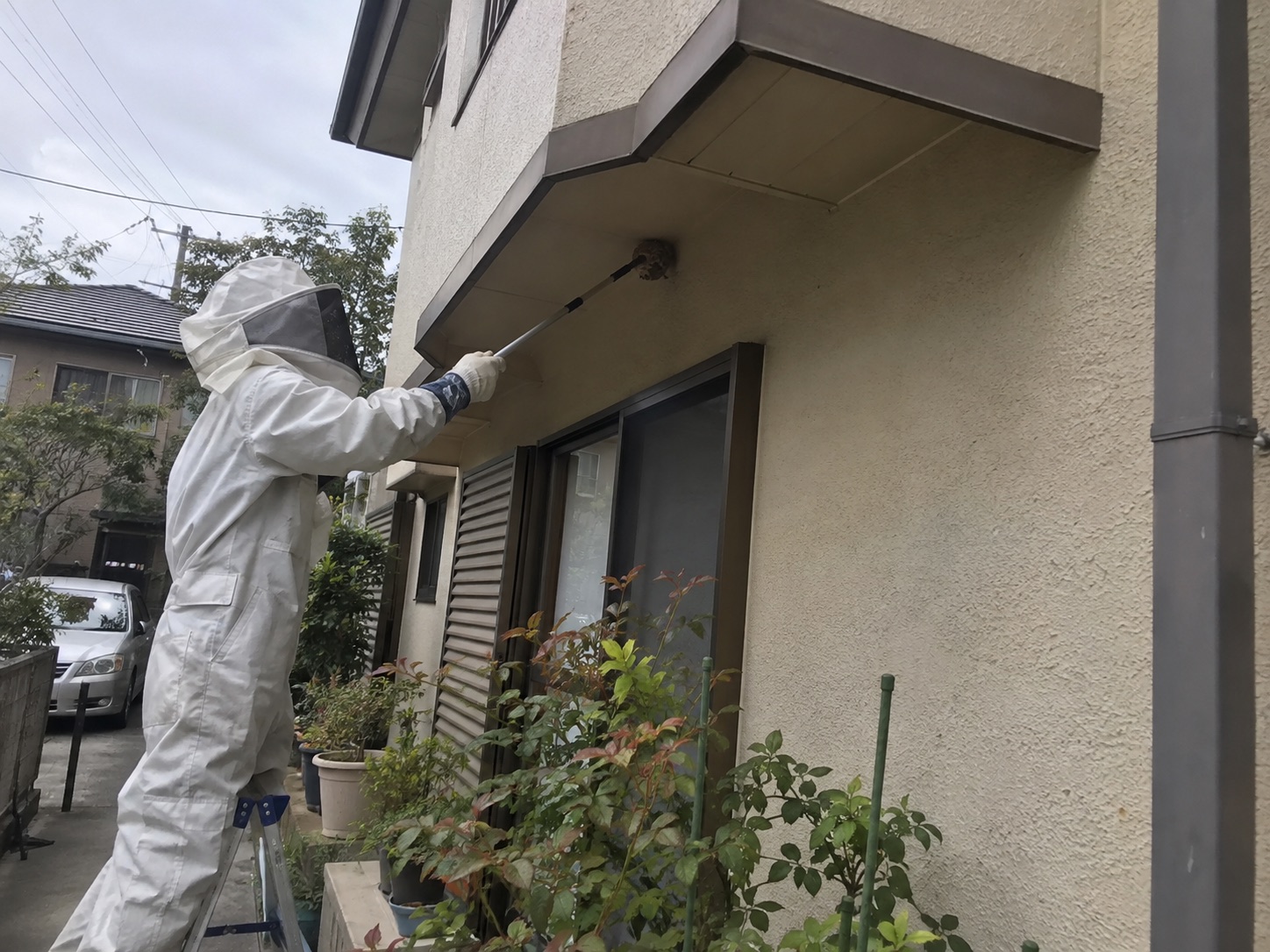 防護服でベランダ下の蜂の巣を処理している作業中の様子