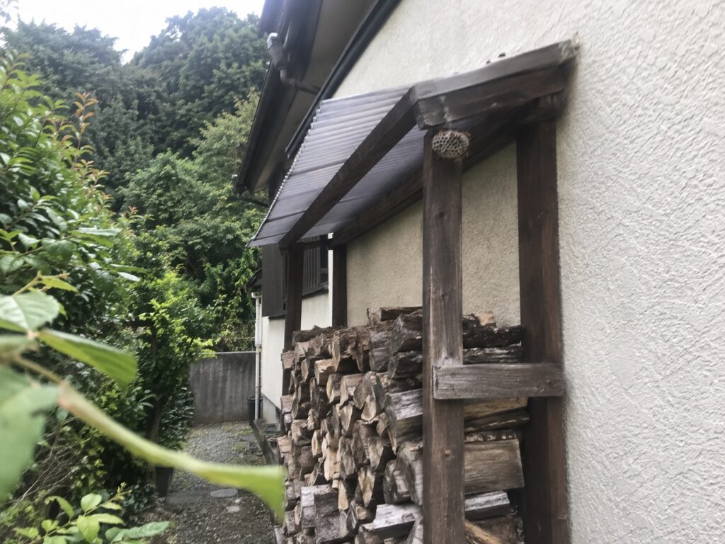 住宅脇の木製薪棚の屋根裏に小さな蜂の巣がある全体状況