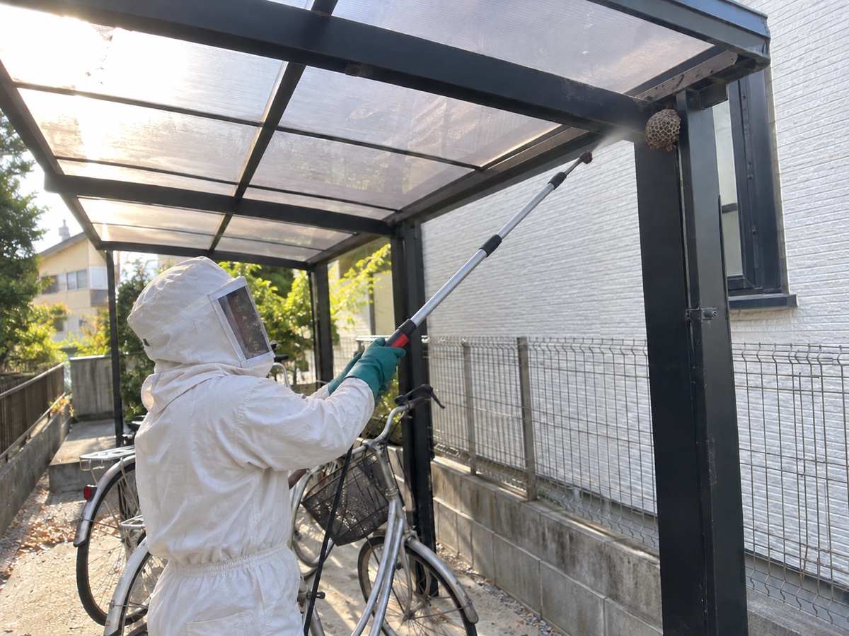 防護服の作業員が駐輪場から距離を取り長い道具で巣を処理する様子